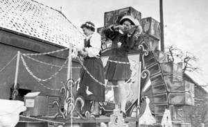 Ein Frau im Gänselieselkostüm und ein Mann im Kostüm eines Spielmanns zusammen auf einem Karnevalswagen