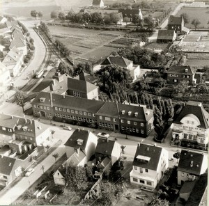 Die heutige Stadtmitte auf einem Luftbild von 1957: Blick auf die Alte Schulstraße mit dem Rathaus und dem damaligen Postamt (am rechten Bildrand), im Hintergrund die Haltestelle der Straßenbahn und das Gelände der Gärtnerei Holthausen. 