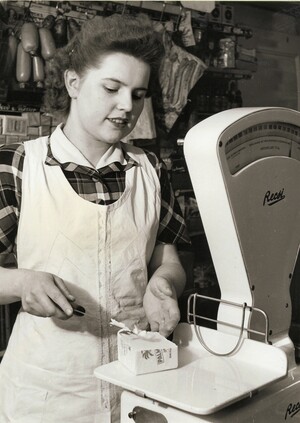 Schwarz-weiß Foto: Eine Frau in einer weißen Schürze schneidet mit einem Messer ein Stück Butter