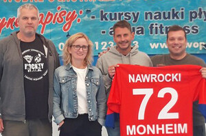 Vier Personen, eine Person hält ein rotes Eishockeytrikot in die Kamera mit der Aufschrift: "Nawrocki 72 Monheim"
