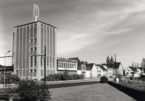 Das alte Gebäude der Brauerei mit großem Pilsglas auf dem Dach, im Hintergrund die Kirchtürme von St. Stephanus