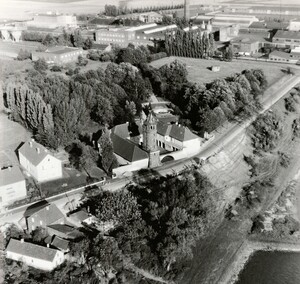 Altes schwarz-weiß Foto: Luftbild auf die Rheinuferstraße in Blee. An der Straße eine Fabrik mit einem runden Turm