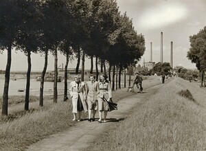 Altes schwarz-weiß Foto: drei Frauen schlendern auf dem Rheindeich, im Hintergrund dreht sich ein Radfahrer in voller Fahrt nach hinten um, im Hintergrund ist die Marienkapelle erkennbar
