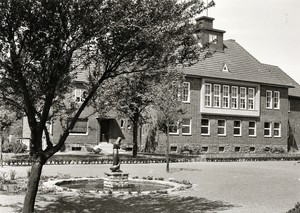 Ein altes schwarz-weiß Foto: Das Rathaus, davor ein kliener runder Brunnen. In der Mitte des Brunnens steht eine kleine Säule aus Stein, darauf die Statue einer Gänseliesel mit zwei Gänsen