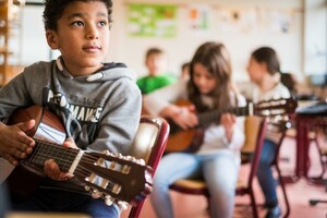 Ein junge mit einer Gitarre, im Hintergrund weitere Kinder mit Instrumenten