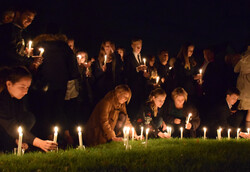 Mehrere Menschen stellen in der Dunkelheit brennende Kerzen auf den Boden