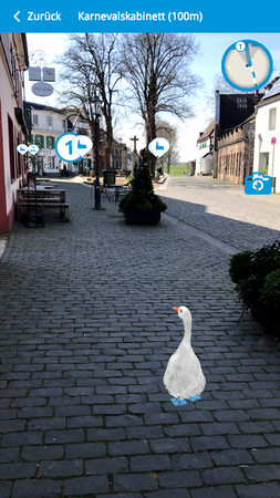 Wenn ein Ziel ausgewählt wurde, wird die App zur sogenannten Augmented-Reality-Anwendung: Direkt vor den eigenen Füßen watschelt die Gans zum Karnevalskabinett. Foto: Screenshot / Stadt Monheim am Rhein