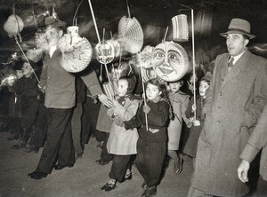 altes schwarz-weiß Foto: Kinder mit altmodischen Laternen, davor zwei Männer mit langen Mänteln und Hut