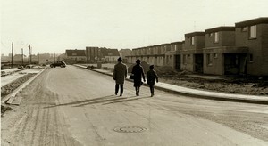 Bild in schwarz-weiß: drei Menschen auf der Geschwister-Scholl-Straße, links von der Straße ist es karg, rechts stehen in eine Reihe neue Einfamilienhäuser