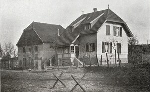 Bild in schwarz-weiß: ein mehrstöckiges Bauernhaus mit eine großen Ziegenweide davor