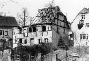 altes schwarz-weiß Foto: ein großes Wohnhaus, das Dach und Teile der Mauern sind zerstört und eingebrochen