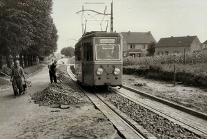 Bild in schwarz-weiß: ein kleiner Straßenbahnwagen auf Schienen, danneben schütten Bauarbeiter grobe Steine auf