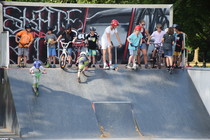 Viele Kinder mit Rollern, Skateboards oder Rollschuhen auf einer Rampe im Skatepark