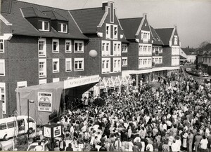 Schwarz-weiß Foto der Eröffnung des ersten Bauabschnitss: Menschenmaßen drängen sich vor einer kleinen Bühne im Monheimer Zentrum