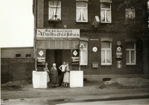 Ein altes schwarz-weiß Foto des "Waldschlösschens" an der Opladener Straße. Im Eingang der Gaststätte stehen mehrere Besucher