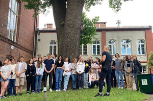 Gruppenfoto von etwa 30 Schülerinnen und Schülern des Otto-Hahn-Gymnasiums vorm Liceum Ogólnokształcące in Malbork. Das Gebäude besteht aus hellem Putz und roten Backsteinen. Davor steht ein großer Baum.