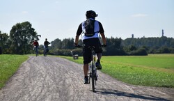 Eine Person auf dem Rad, im Hintergrund Wege, Wiesen und Bäume