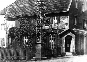 Ein schwarz-weiß Foto der Antonius-Drogerie, vor dem Haus ein turmartiger Strommast, der gleichzeitig als Straßenbeleuchtung diente