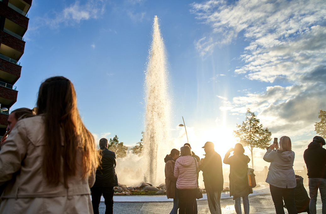 Der Monheimer Geysir spritzt eine Wasserfontäne in die Luft, davor einige Menschen