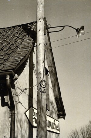 Altes schwarz-weiß Foto: ein Holzmast, daran eine einfache Lampe mit einer Glühbirne